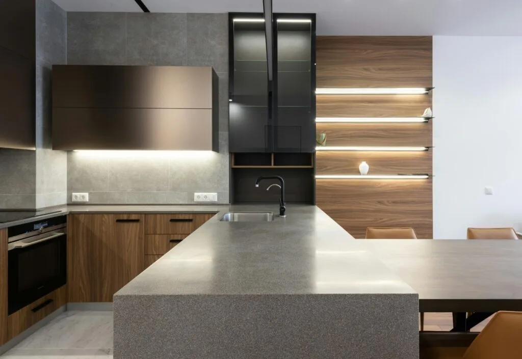 Wooden cupboards with stove placed near gray counter in modern kitchen with light decoration on wall and table in apartment